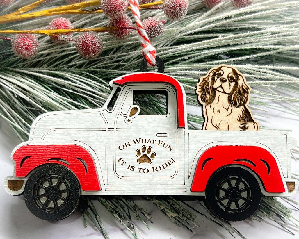 A vintage style red and white truck ornament with a dog riding in the back seat, placed on a branch with Christmas decorations.