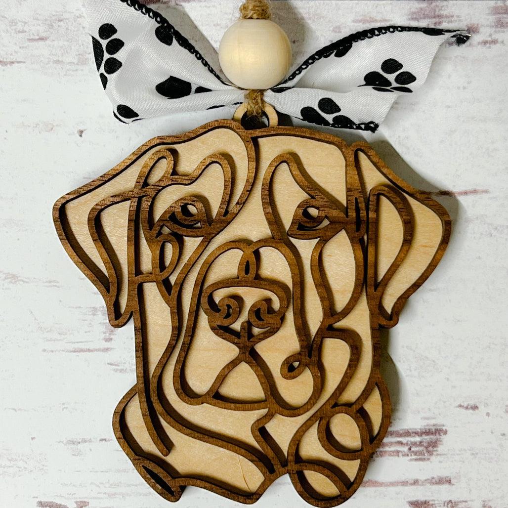 Laser-cut wooden doodle art dog ornament with paw print ribbon bow and bead, hanging on rustic twine.