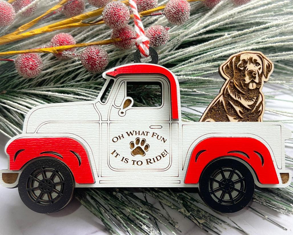 A vintage style red and white truck ornament with a dog riding in the back seat, placed on a branch with Christmas decorations.