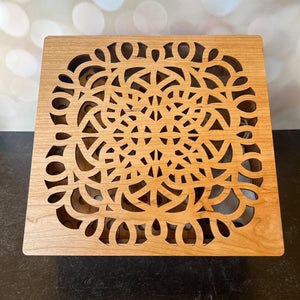 Wooden square coaster with intricate cut-out design on a dark surface.