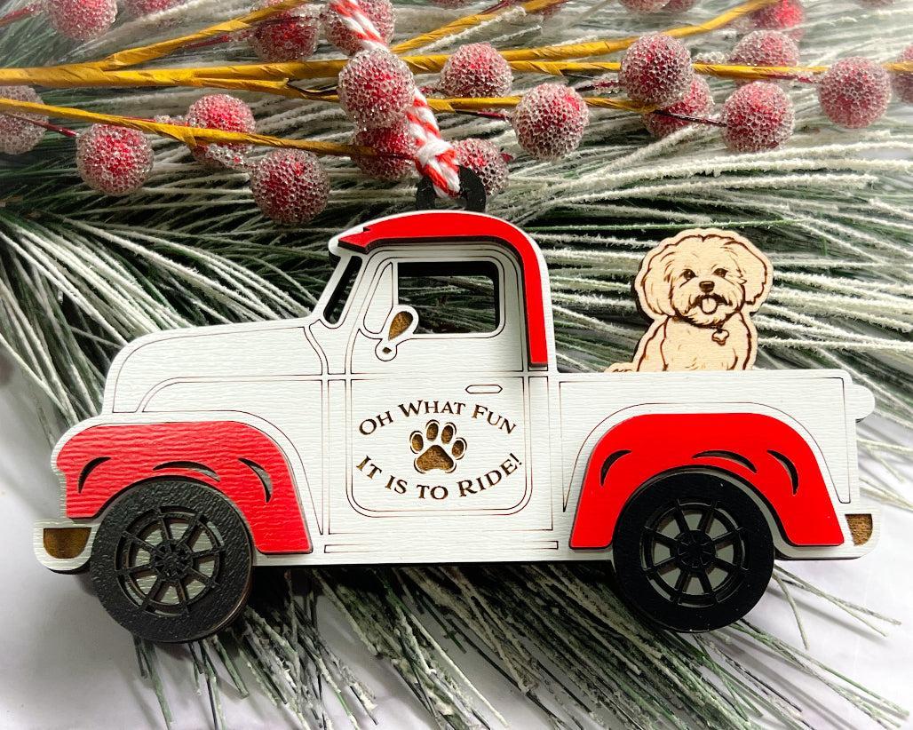 A vintage style red and white truck ornament with a dog riding in the back seat, placed on a branch with Christmas decorations.