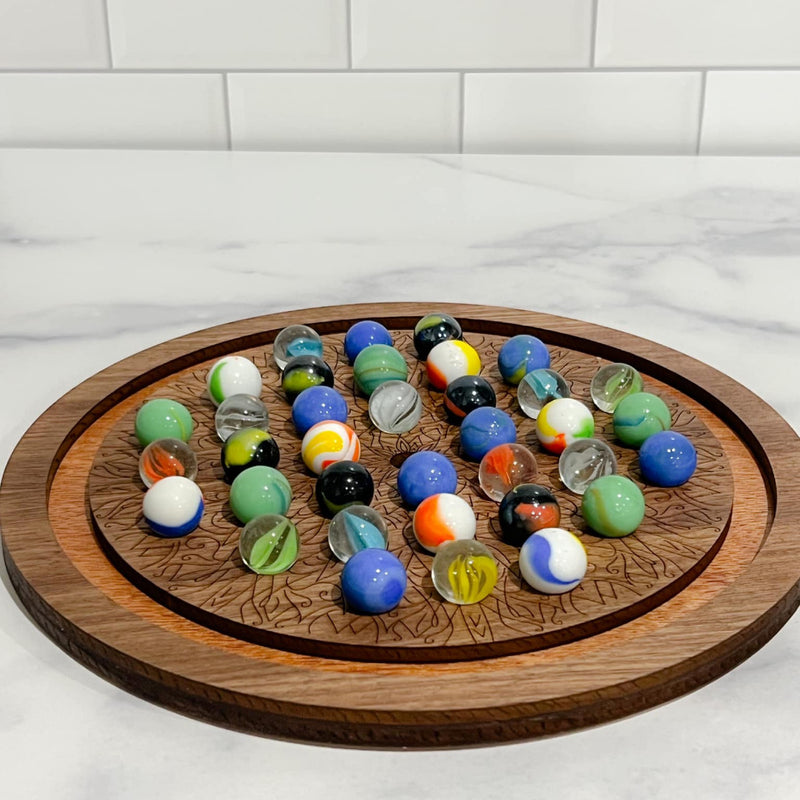 A wooden solitaire marble game with a circular board and various colored marbles placed on it, set against a marble-tiled surface.