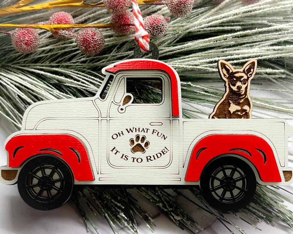 A vintage style red and white truck ornament with a dog riding in the back seat, placed on a branch with Christmas decorations.