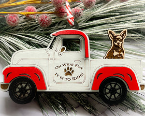 A vintage style red and white truck ornament with a dog riding in the back seat, placed on a branch with Christmas decorations.
