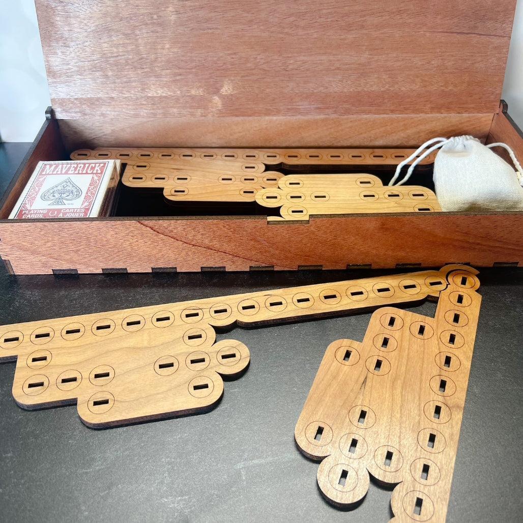 Wooden cribbage board set with cards and dice bag on a gray surface.