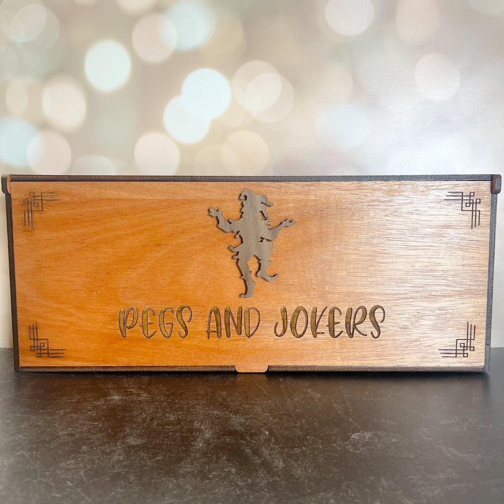 Wooden box with 'Pegs and Jokers' engraving on a blurred background
