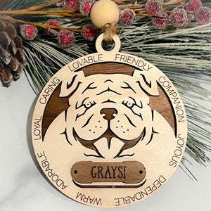 Wooden dog ornament with engraved bulldog face, surrounding words like “loyal, lovable, friendly,” and custom nameplate reading “Graysi,” finished with bead and twine hanger.
