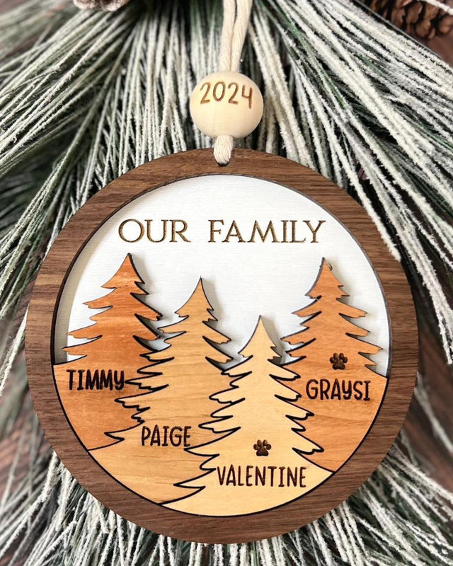 Round wooden family ornament with layered trees engraved with names Timmy, Paige, Valentine, and Graysi, “Our Family” text, and 2024 bead hanging on frosted greenery.