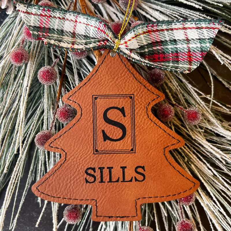 Brown leatherette tree ornament with greenery and berry background