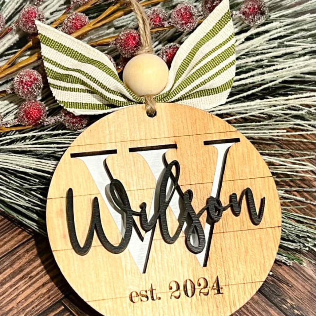 A personalized wooden name ornament with the name 'Wilson' and the year '2024' inscribed on a circular wooden tag, adorned with a decorative leaf and berry accents.