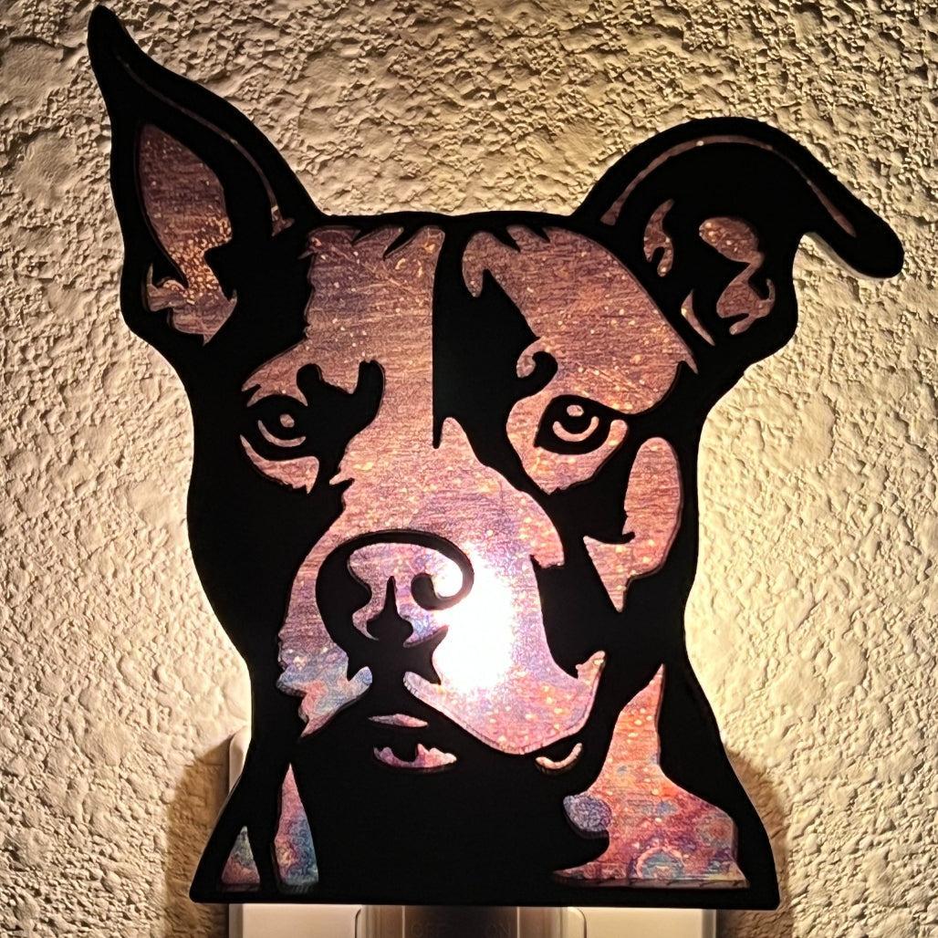 A laser-cut wooden night light in the shape of a dog's head, glowing with a warm light.