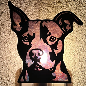 A laser-cut wooden night light in the shape of a dog's head, glowing with a warm light.