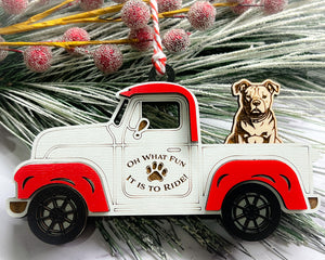 A vintage style red and white truck ornament with a dog riding in the back seat, placed on a branch with Christmas decorations.