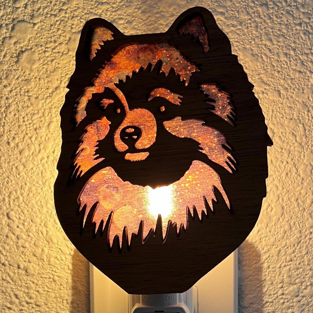 A laser-cut wooden night light in the shape of a dog's head, glowing with a warm light.