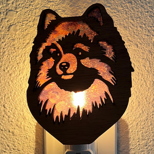 A laser-cut wooden night light in the shape of a dog's head, glowing with a warm light.