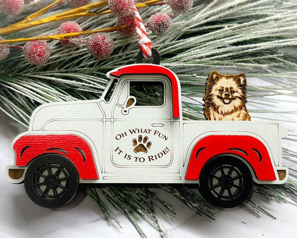 A vintage style red and white truck ornament with a dog riding in the back seat, placed on a branch with Christmas decorations.