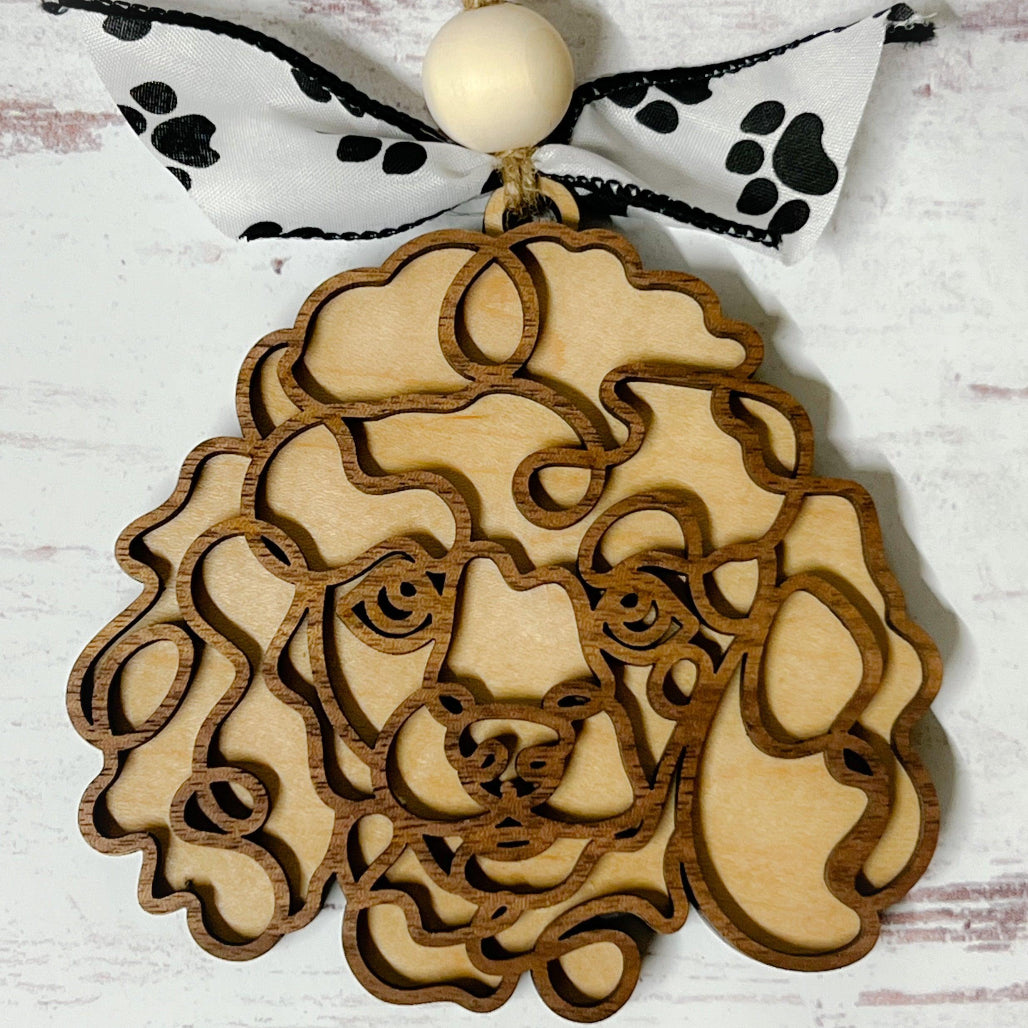 Laser-cut wooden doodle art dog ornament with paw print ribbon bow and bead, hanging on rustic twine.