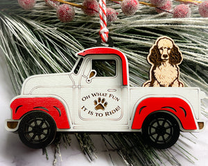 A vintage style red and white truck ornament with a dog riding in the back seat, placed on a branch with Christmas decorations.