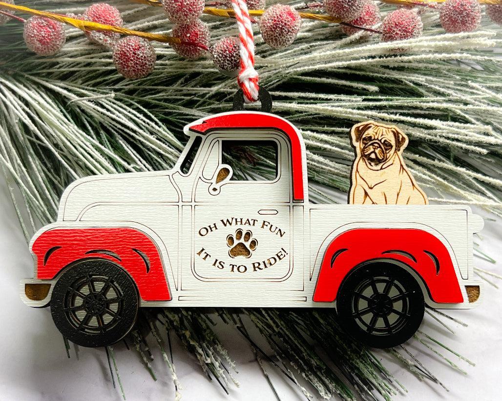 A vintage style red and white truck ornament with a dog riding in the back seat, placed on a branch with Christmas decorations.