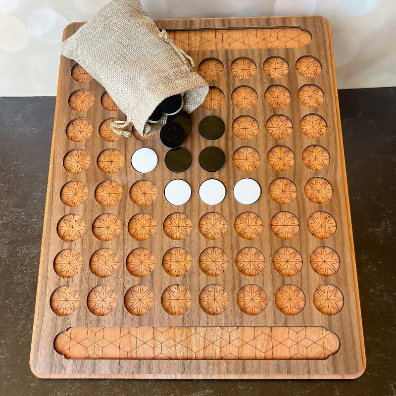 Wooden game board with circular holes and a bag of black and white stones on a dark surface.