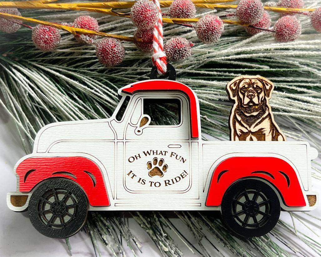 A vintage style red and white truck ornament with a dog riding in the back seat, placed on a branch with Christmas decorations.