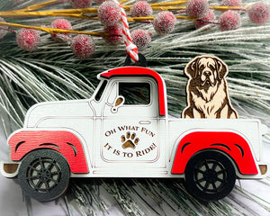 A vintage style red and white truck ornament with a dog riding in the back seat, placed on a branch with Christmas decorations.