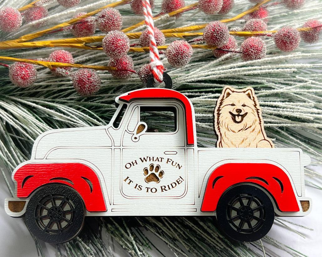 A vintage style red and white truck ornament with a dog riding in the back seat, placed on a branch with Christmas decorations.