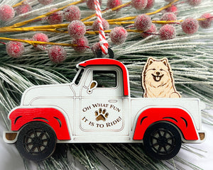A vintage style red and white truck ornament with a dog riding in the back seat, placed on a branch with Christmas decorations.