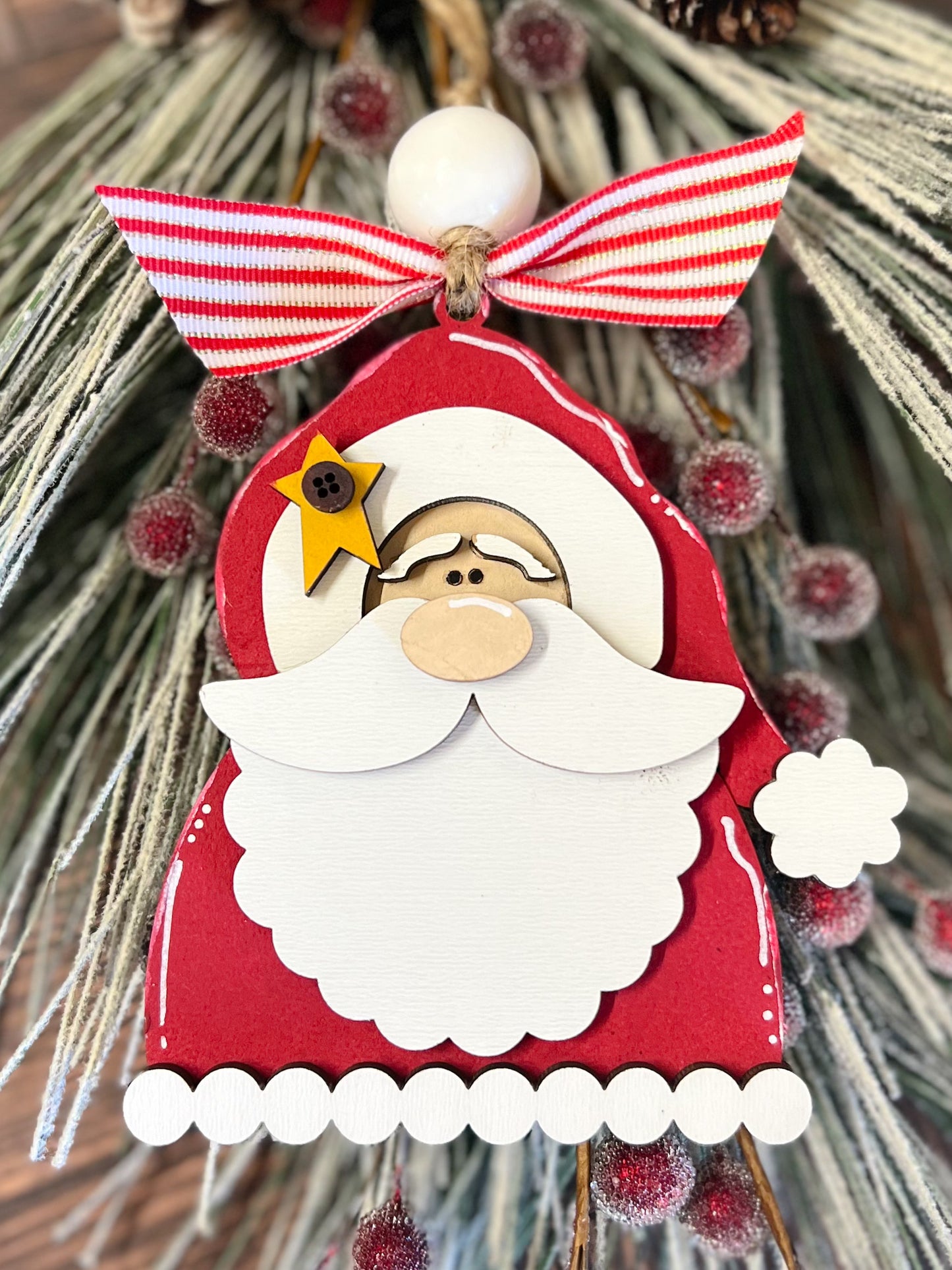 A wooden laser-cut Santa ornament with a red and white striped ribbon and white bead decorations.