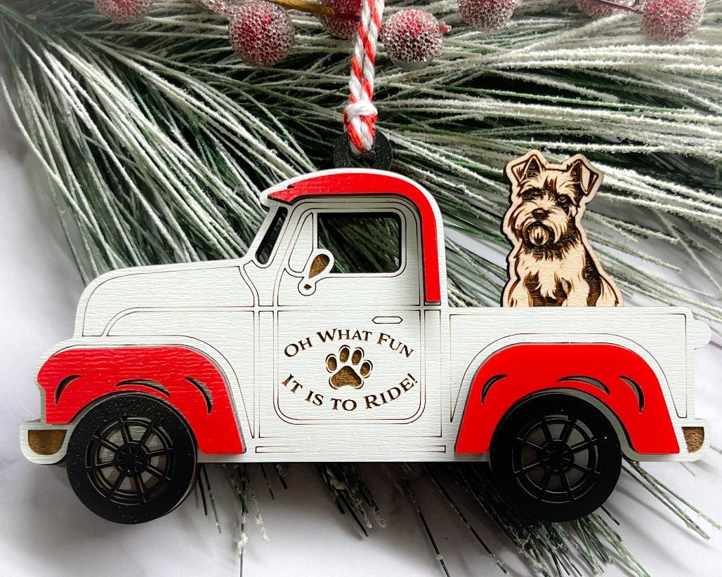 A vintage style red and white truck ornament with a dog riding in the back seat, placed on a branch with Christmas decorations.