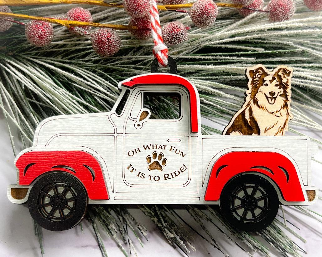 A vintage style red and white truck ornament with a dog riding in the back seat, placed on a branch with Christmas decorations.