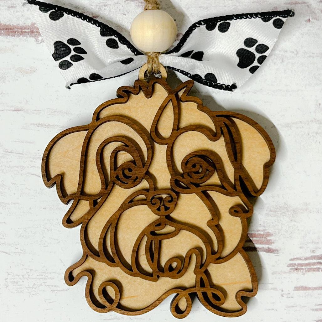 A wooden ornament in the shape of a doodle art depiction of a dog breed, with a paw print ribbon and bead decorations.