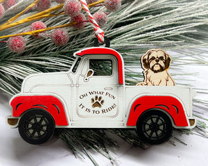 A vintage style red and white truck ornament with a dog riding in the back seat, placed on a branch with Christmas decorations.
