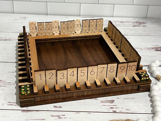 A wooden 'Shut the Box' game board set on a white surface with wooden pieces shaped as numbers and decorative dice on the board.
