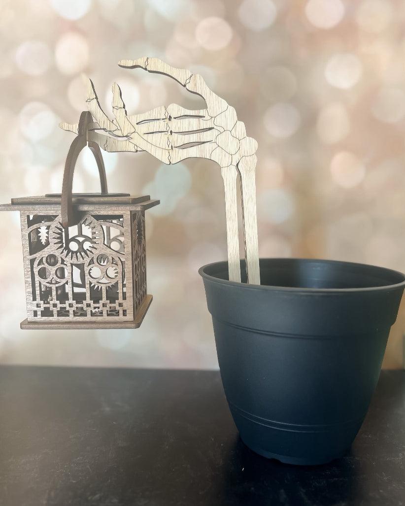 Wooden skeleton hand lantern holder displayed in a black pot (pot not included).