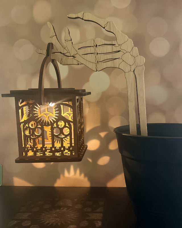 Skeleton hand lantern holder glowing in the dark with spooky cutout designs casting shadows.