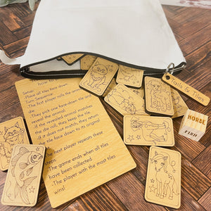 The image shows a memory matching game called Tails & Tiles, consisting of wooden tiles with animal illustrations, a wooden die, and an instruction card, all displayed on a wooden table.