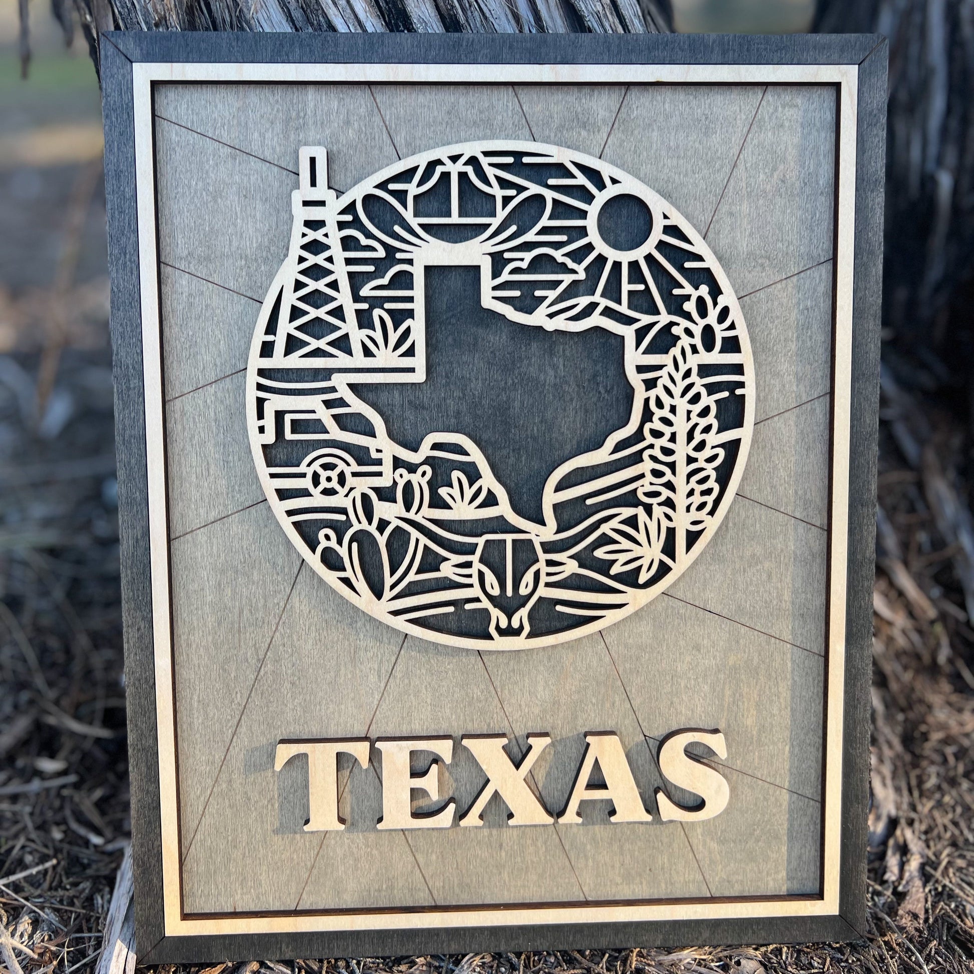 A laser-cut wooden sign or ornament with a silhouette of Texas and iconic symbols, including an oil rig, desert cacti, and the Texas sun. The word 'TEXAS' is prominently displayed at the bottom.