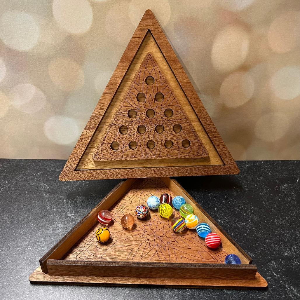 Wooden triangle-shaped game board with colorful marbles on a dark surface and blurred light background