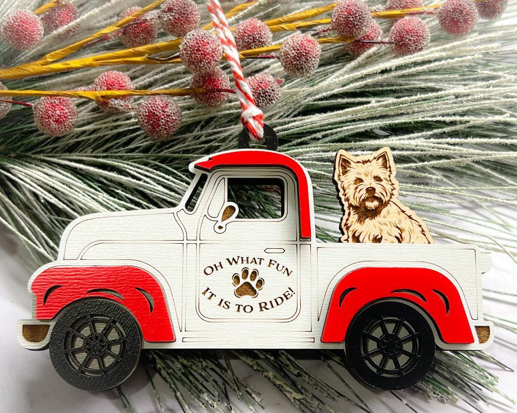 A vintage style red and white truck ornament with a dog riding in the back seat, placed on a branch with Christmas decorations.
