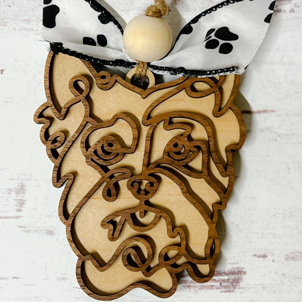 Laser-cut wooden doodle art dog ornament with paw print ribbon bow and bead, hanging on rustic twine.