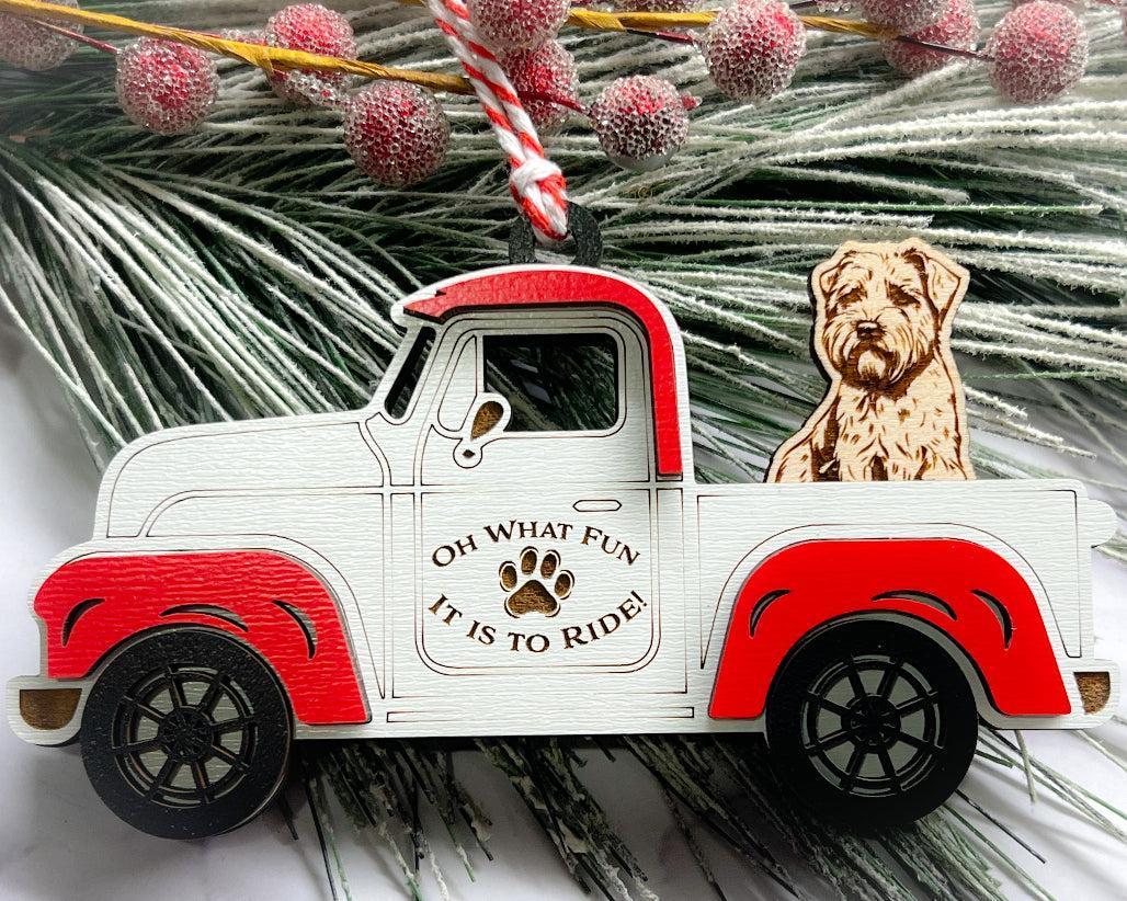 A vintage style red and white truck ornament with a dog riding in the back seat, placed on a branch with Christmas decorations.
