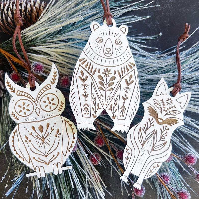 Decorative animal ornaments (bear, owl, and fox) with intricate patterns hanging on a branch.