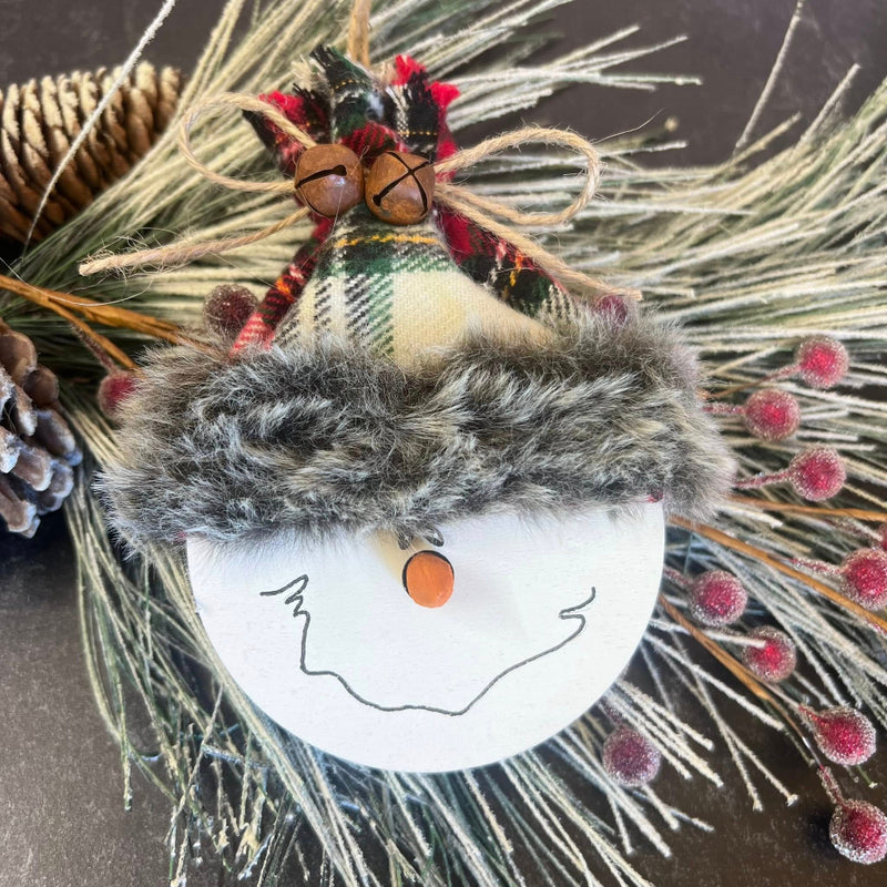 Decorative wreath with a small figure, plaid fabric, and natural elements on a dark background.