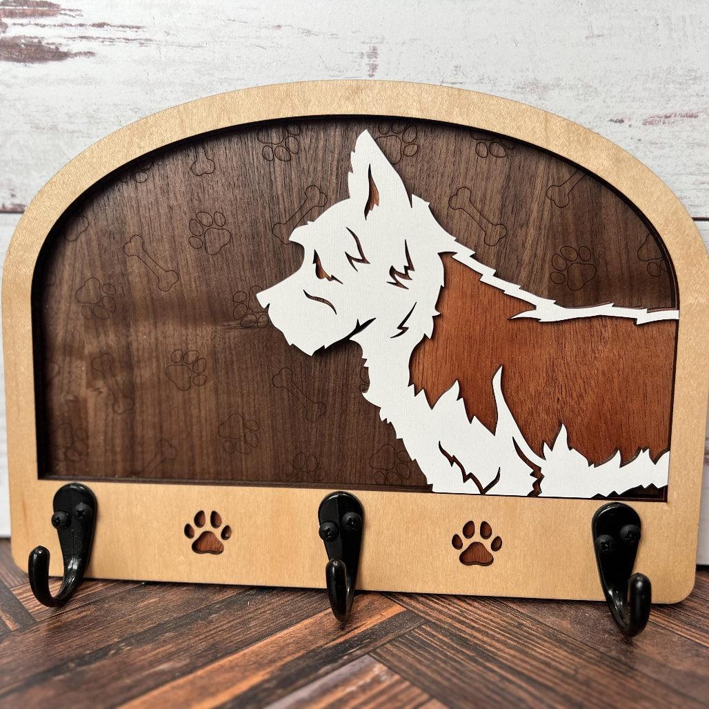 A wooden dog leash holder with a cut-out silhouette of a dog and the phrase 'Unleash Adventure'. It features three hooks at the bottom and paw prints around the dog's silhouette.