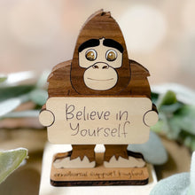 Load image into Gallery viewer, Wooden figure of Bigfoot holding a sign with 'Believe in Yourself' text, surrounded by greenery.