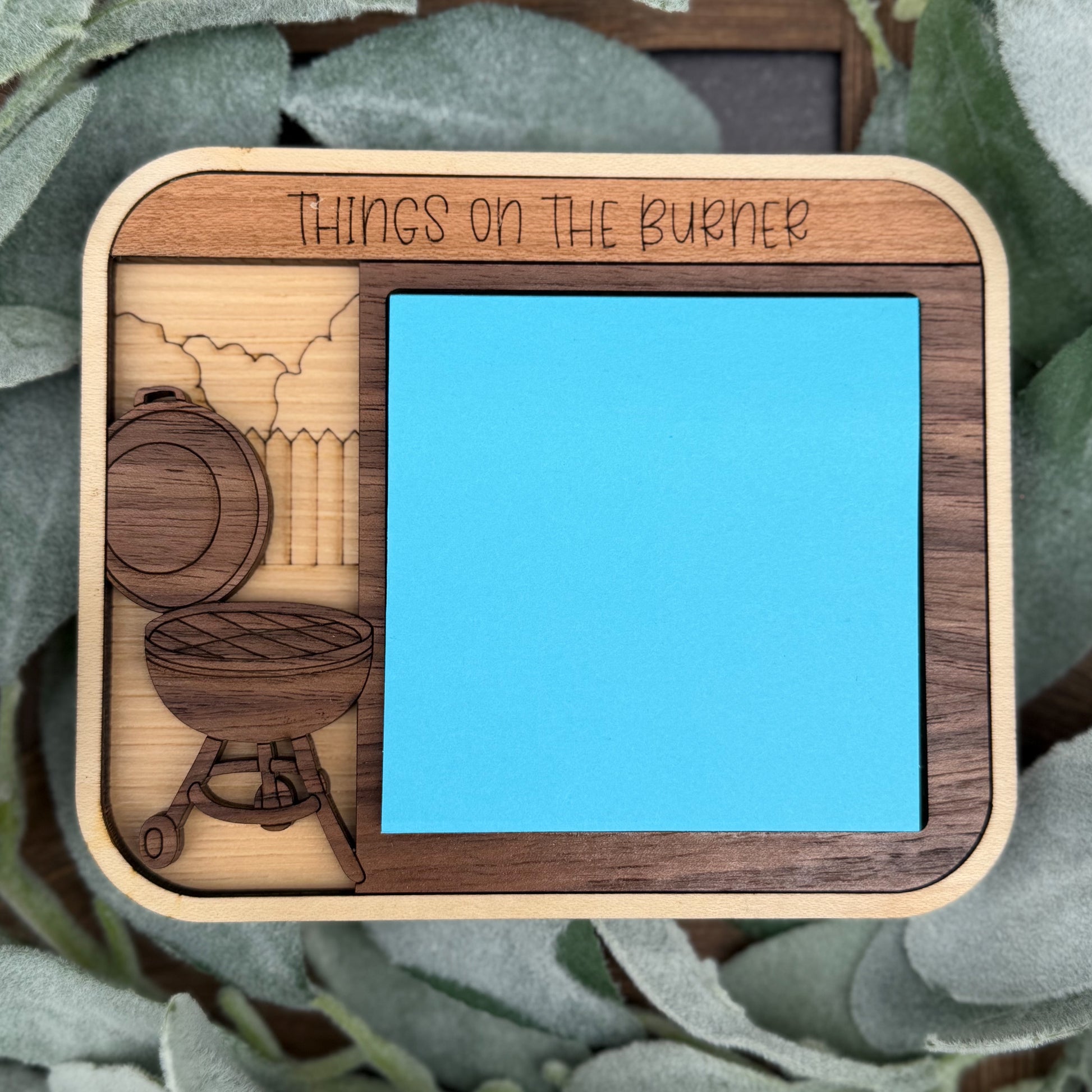 Wooden tray with engraved designs and 'Things on the Burner' text, surrounded by green leaves.