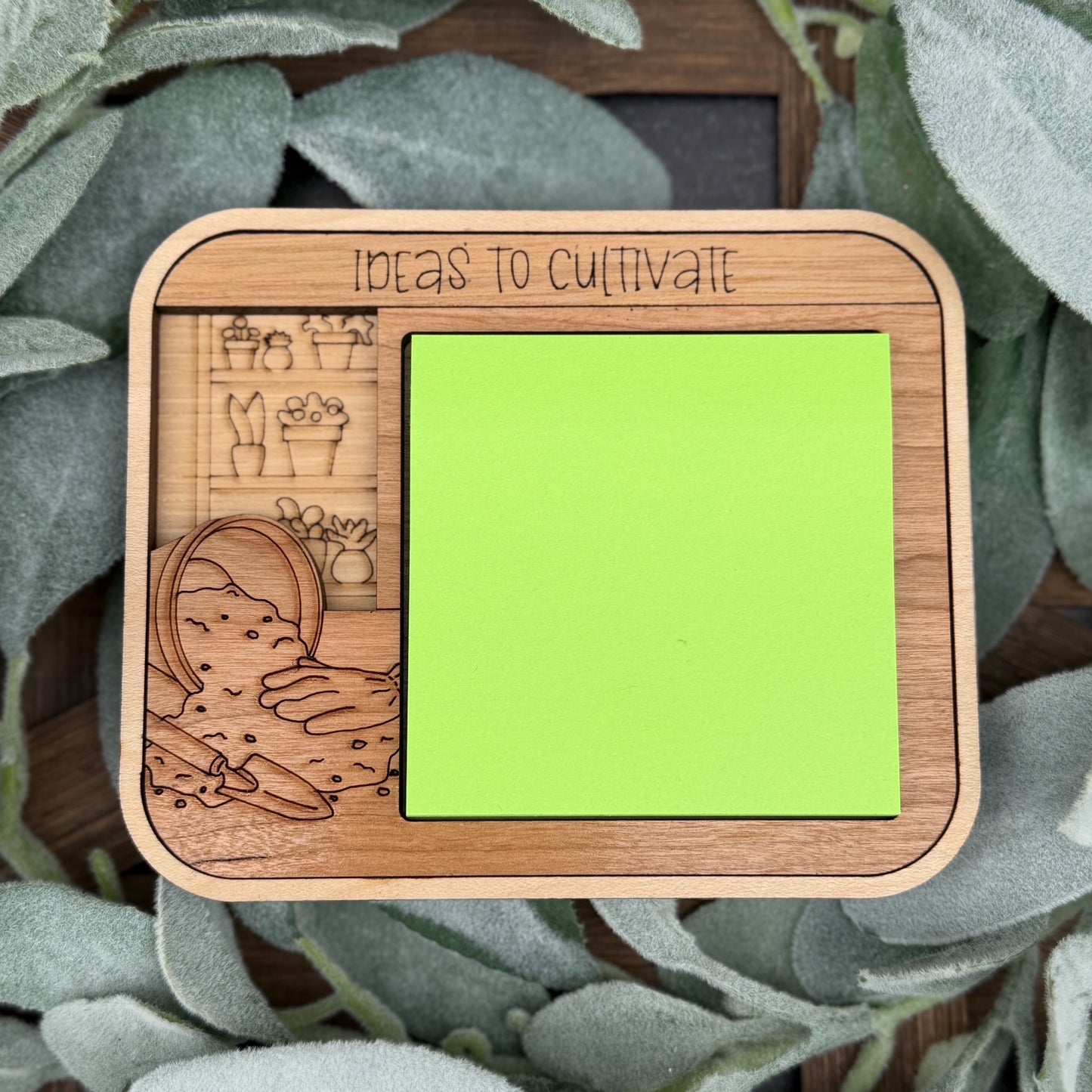 Wooden frame with green sticky note and engraved illustrations on a leafy background