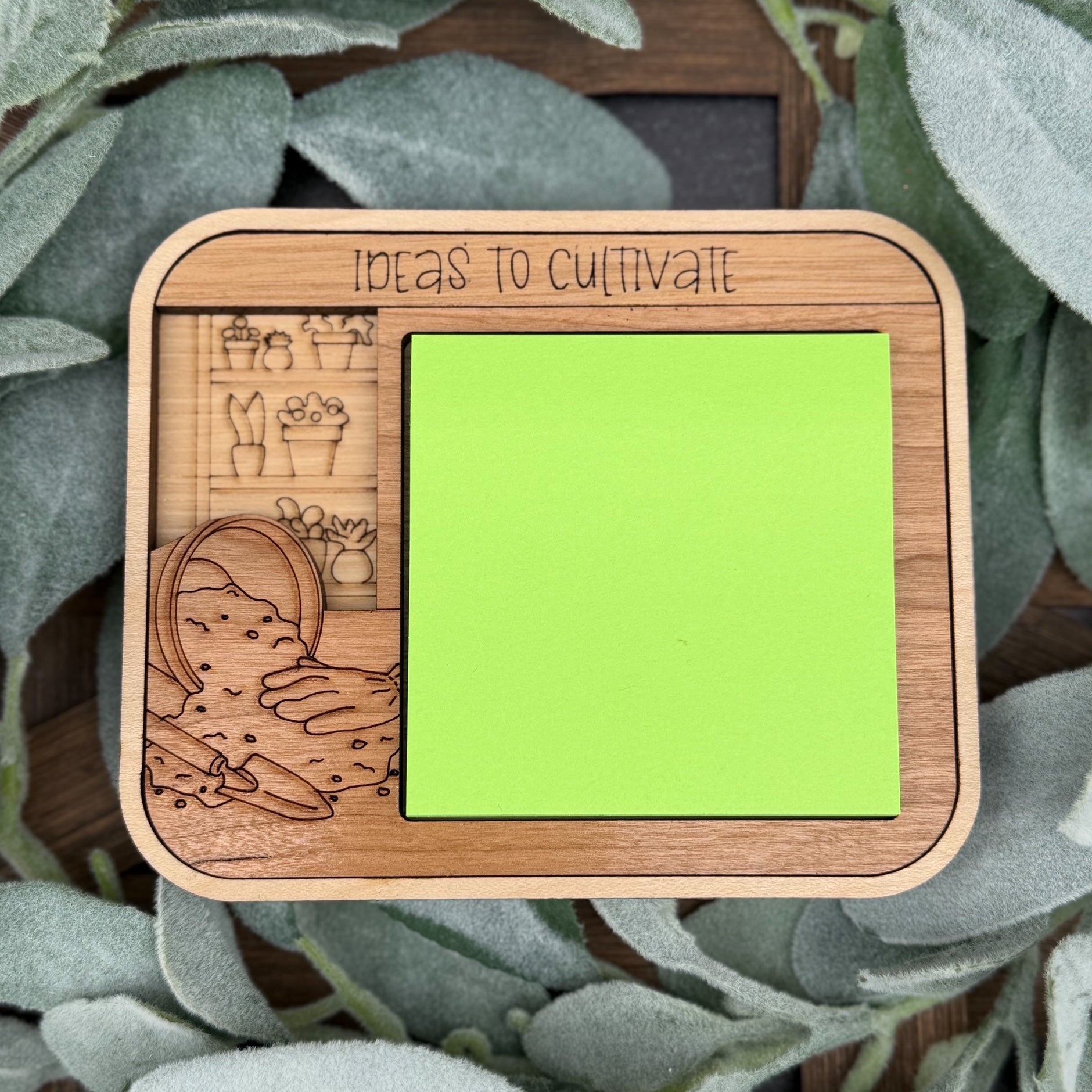 Wooden frame with green sticky note and engraved illustrations on a leafy background