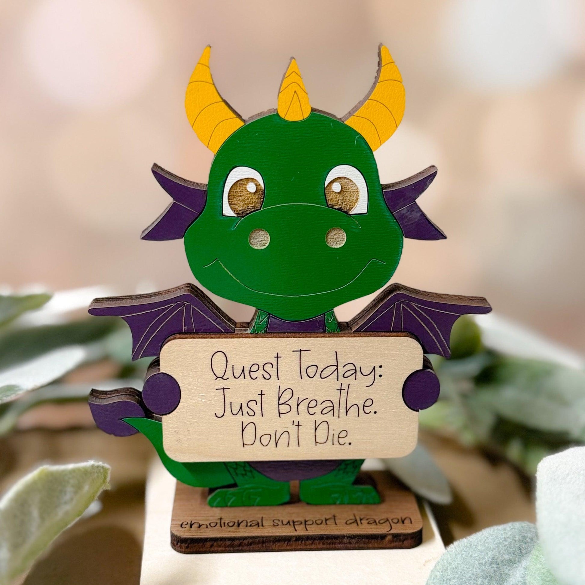 Decorative dragon figurine holding a sign with motivational quote, surrounded by plants.